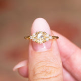 Antique-inspired primrose yellow diamond cluster tre-foil engagement ring held between fingers with oval yellow diamond centre stone.