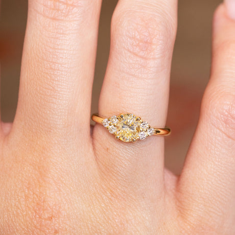 Antique-inspired primrose yellow diamond cluster tre-foil engagement ring with oval yellow diamond centre stone worn on finger.