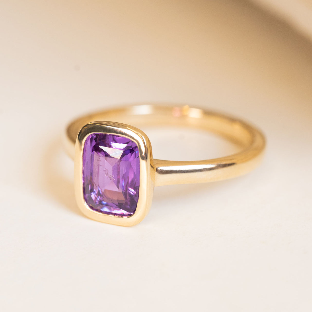 Royal purple cushion-cut sapphire solitaire engagement ring with a polished yellow gold band.