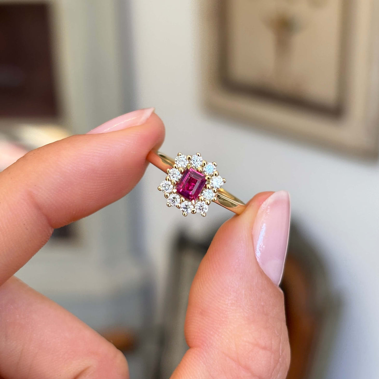 Rectangular step-cut ruby and diamond cluster engagement ring showcasing a rectangular step-cut ruby and diamond halo, held by hand.