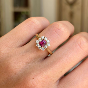 Rectangular step-cut ruby and diamond cluster engagement ring featuring a rectangular step-cut ruby encircled by diamonds, worn on a hand.