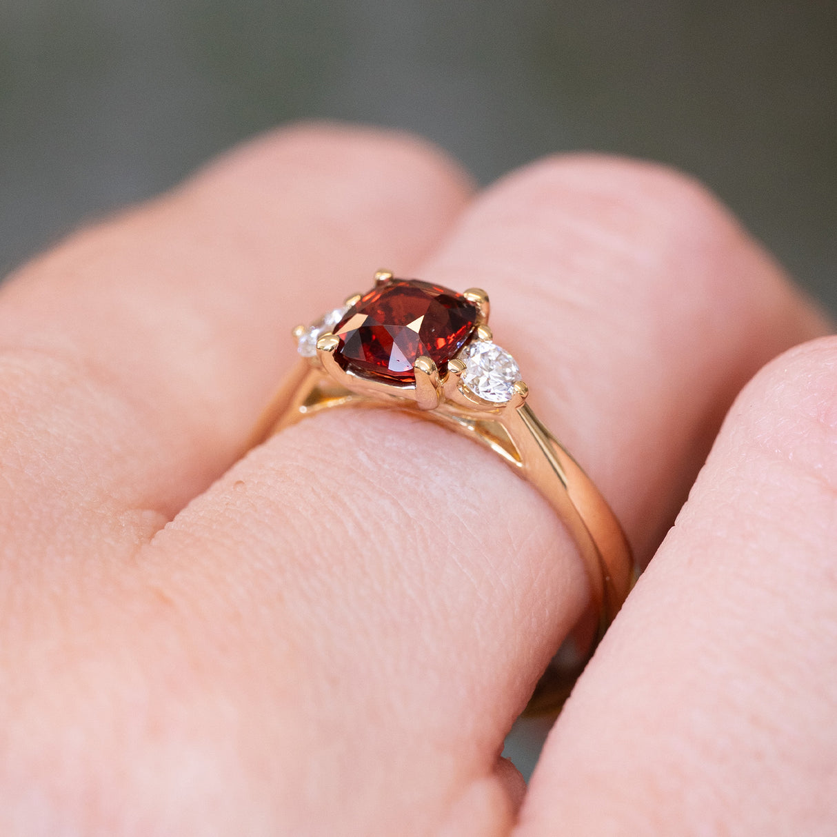 Red spinel and diamond three-stone engagement ring with gold setting and diamond side stones.