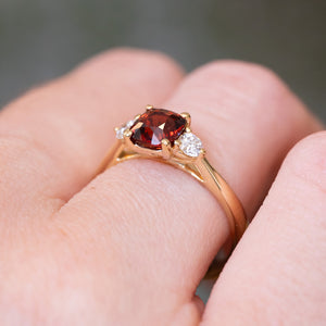 Red spinel and diamond three-stone engagement ring with gold setting and diamond side stones.