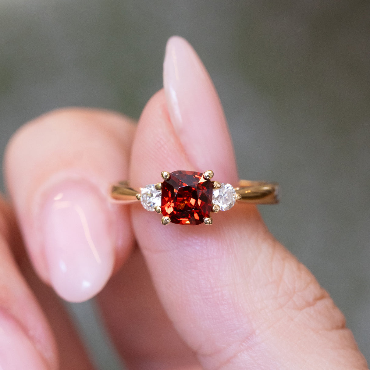 Red spinel and diamond three-stone engagement ring with cushion-cut red spinel centre stone.