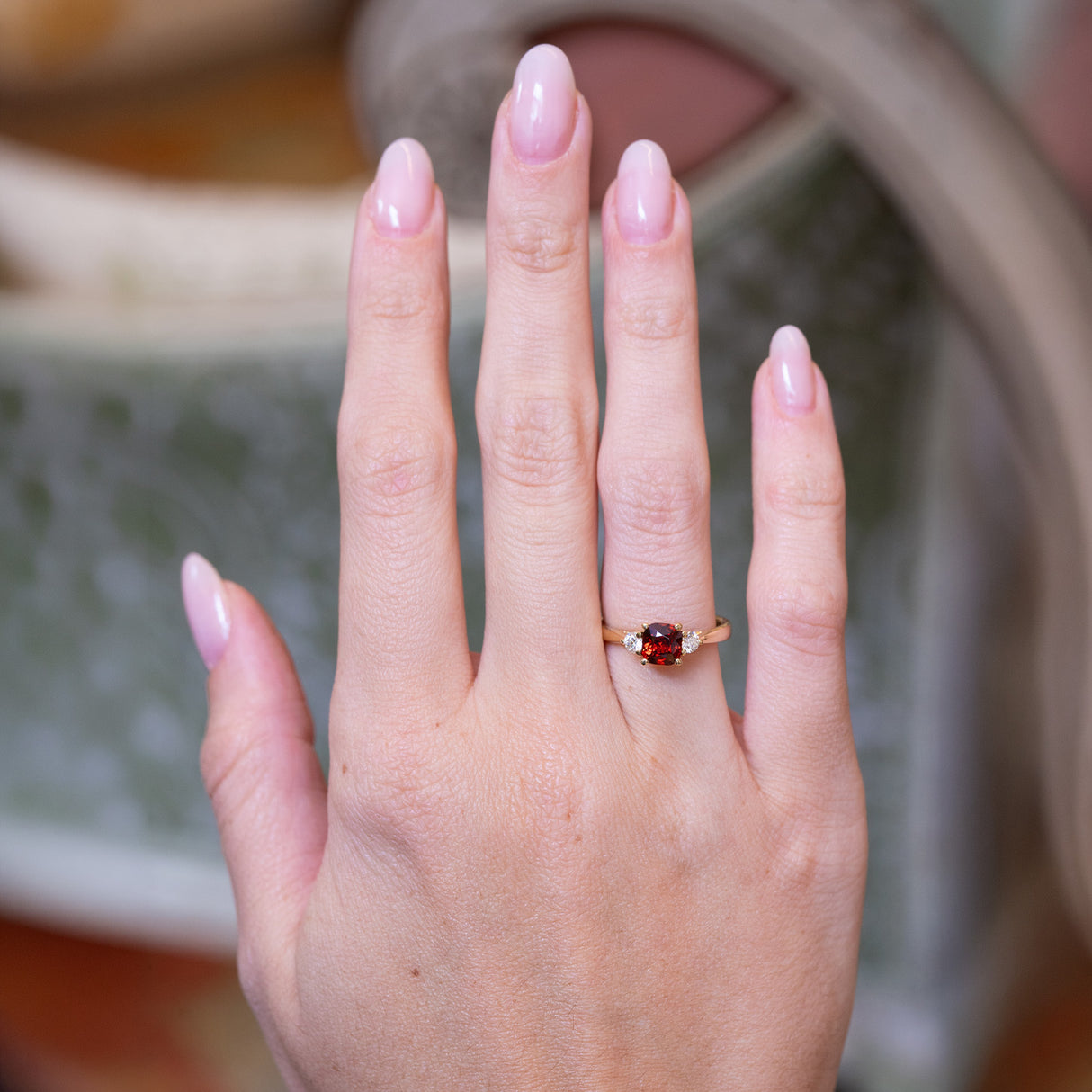 Red spinel and diamond three-stone engagement ring worn on hand with gold band.