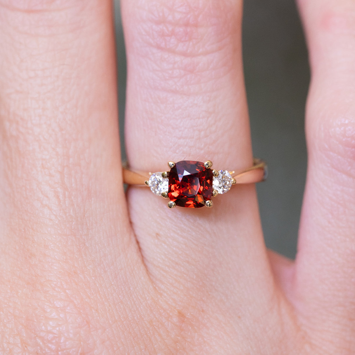 Red spinel and diamond three-stone engagement ring with cushion-cut centre stone worn on finger.