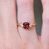 Red spinel and diamond three-stone engagement ring with cushion-cut centre stone worn on finger.