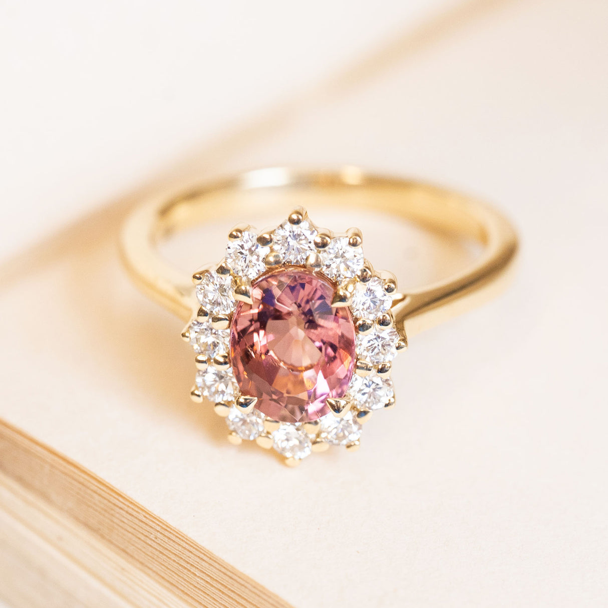 Rose-pink tourmaline engagement ring surrounded by a diamond cluster in yellow gold.
