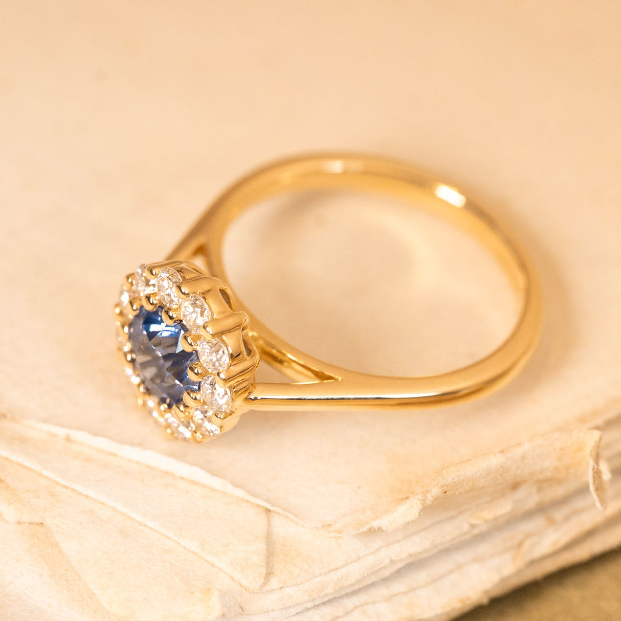 Blue sapphire and diamond cluster engagement ring with a vibrant round sapphire and dazzling diamond halo set in yellow gold.