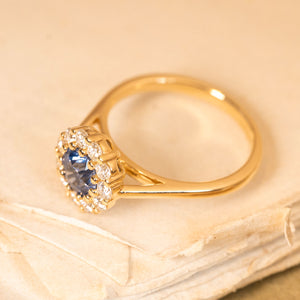 Blue sapphire and diamond cluster engagement ring with a vibrant round sapphire and dazzling diamond halo set in yellow gold.