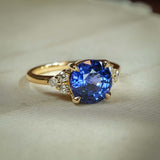 Round blue sapphire engagement ring with diamond trefoil side clusters in yellow gold