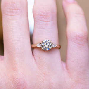 Round brilliant-cut diamond three-stone engagement ring with central round diamond worn on finger.