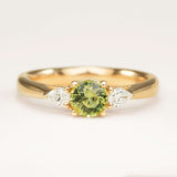 Round-cut green sapphire and diamond three-stone engagement ring in yellow gold with pear-shaped side diamonds.