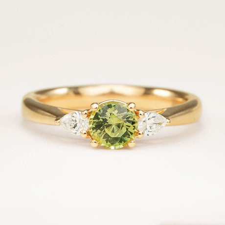 Round-cut green sapphire and diamond three-stone engagement ring in yellow gold with pear-shaped side diamonds.