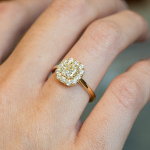 Diamond cluster engagement ring with round brilliant centre stone and clustered diamond surround worn on hand.