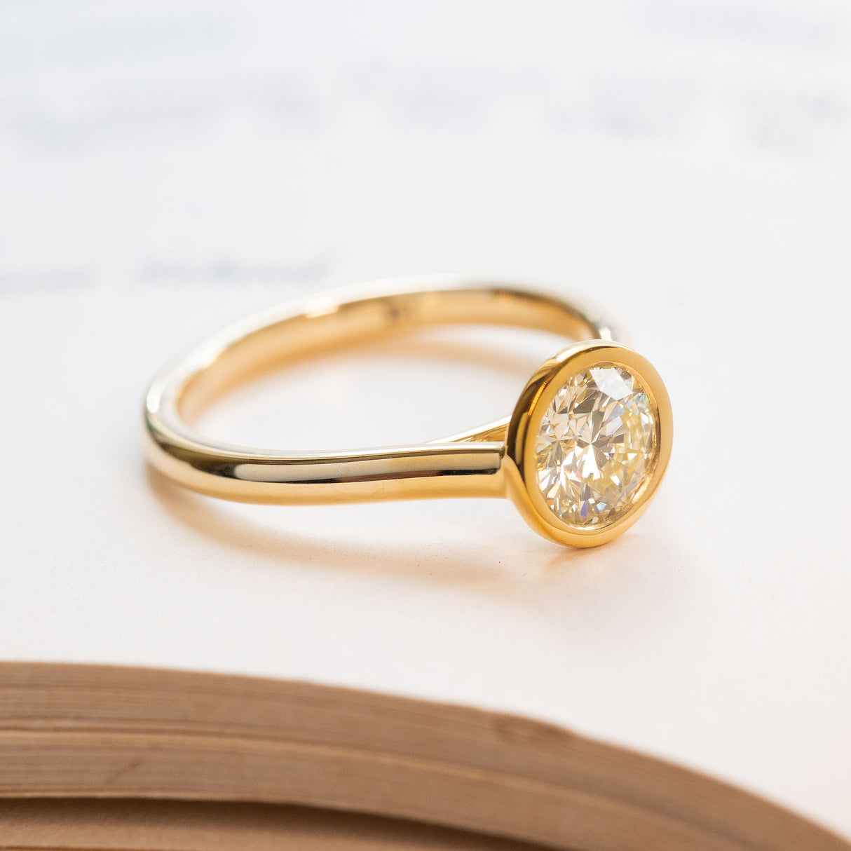 Round brilliant-cut diamond rub-over solitaire engagement ring in yellow gold.