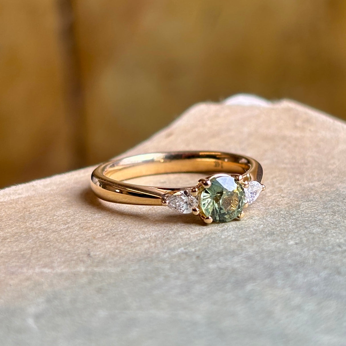 Angled view of round green sapphire three-stone engagement ring with diamond accents in yellow gold.