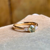 Angled view of round green sapphire three-stone engagement ring with diamond accents in yellow gold.
