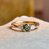 Close-up of round green sapphire engagement ring with diamond side stones in polished yellow gold.