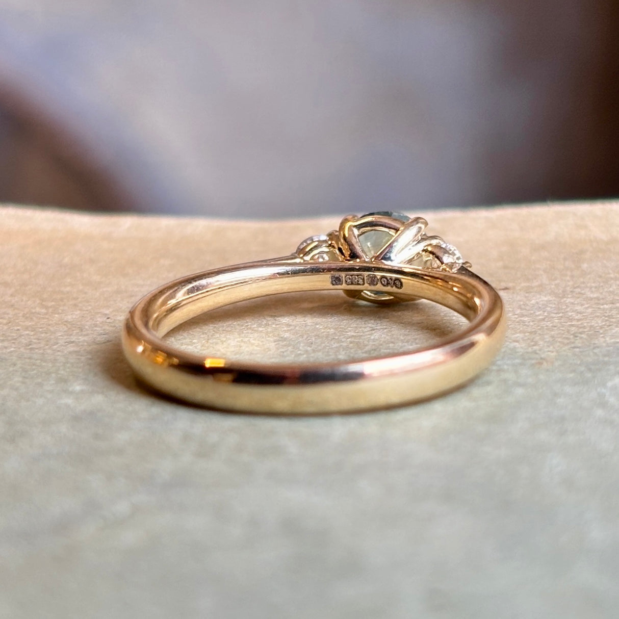 Yellow gold setting of a round teal-green sapphire and diamond three-stone engagement ring.