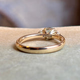 Yellow gold setting of a round teal-green sapphire and diamond three-stone engagement ring.