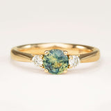 Round teal-green sapphire and diamond three-stone engagement ring in yellow gold.