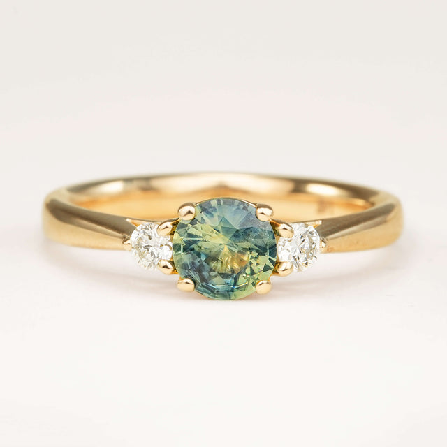 Round teal-green sapphire and diamond three-stone engagement ring in yellow gold.