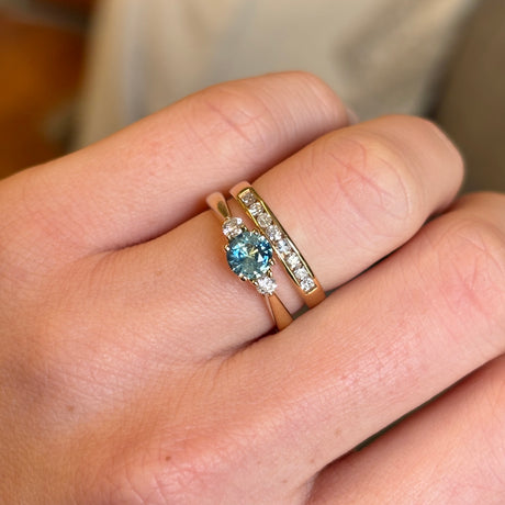 Round teal-green sapphire three-stone engagement ring styled with a yellow gold wedding band.