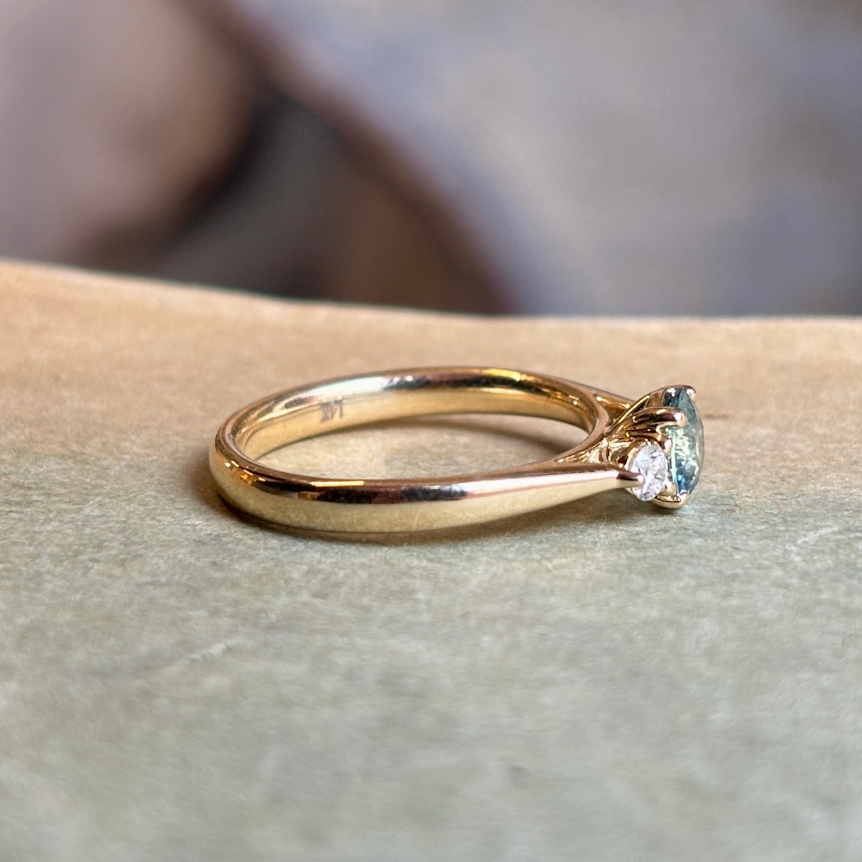 Yellow gold three-stone engagement ring with round teal-green sapphire centre and diamond side stones.