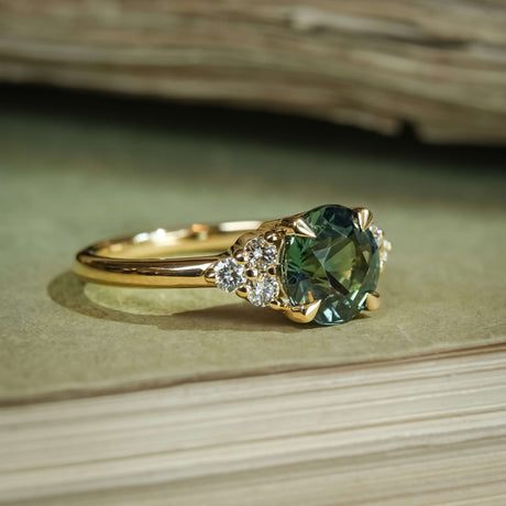 Round teal sapphire engagement ring with diamond trefoil side clusters