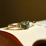 Round teal sapphire and pear diamond three stone engagement ring with yellow gold band