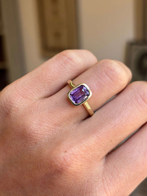 Royal purple cushion-cut sapphire solitaire engagement ring featuring a vibrant cushion-cut purple sapphire in a timeless solitaire design, worn on a hand.