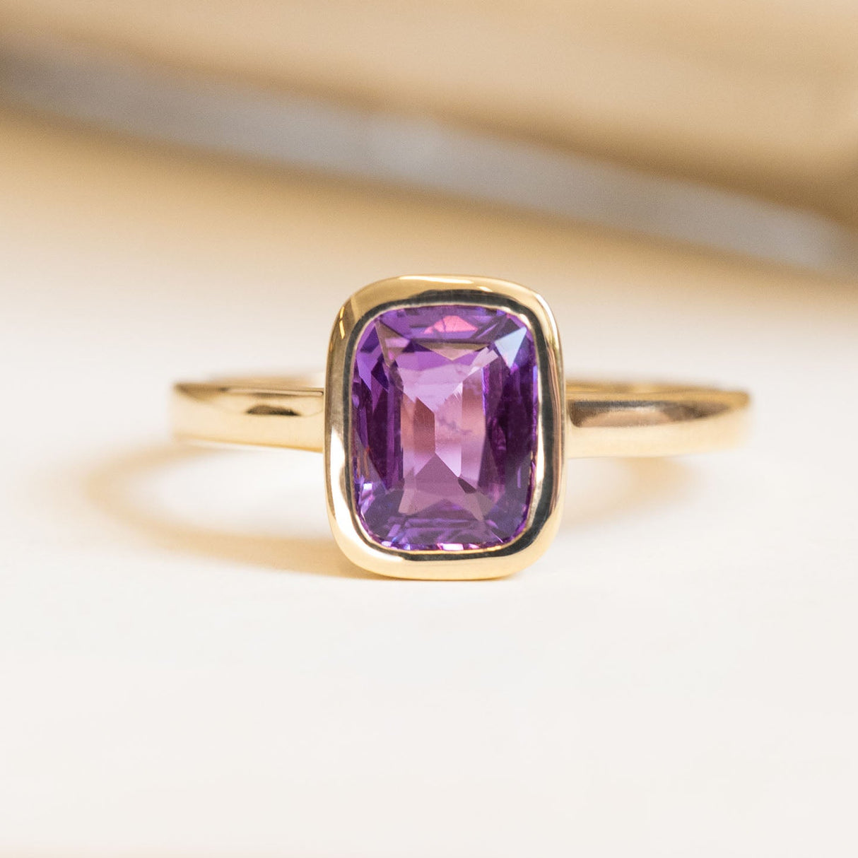 Royal purple cushion-cut sapphire solitaire engagement ring in a yellow gold rub-over setting.