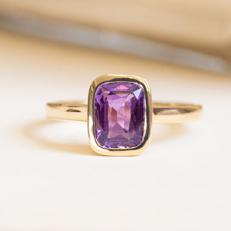 Royal purple cushion-cut sapphire solitaire engagement ring in a yellow gold rub-over setting.