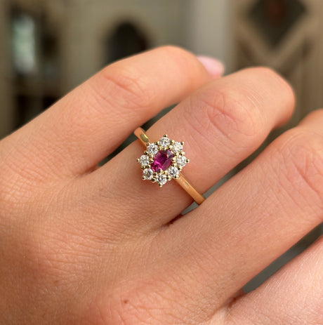 Close-up of an antique-inspired yellow gold cluster ring showcasing an oval-cut ruby encircled by brilliant diamonds, highlighting rich colour and exceptional sparkle.