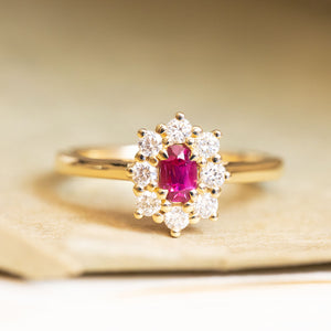 Ruby and diamond cluster engagement ring with an oval ruby centre stone set in yellow gold.
