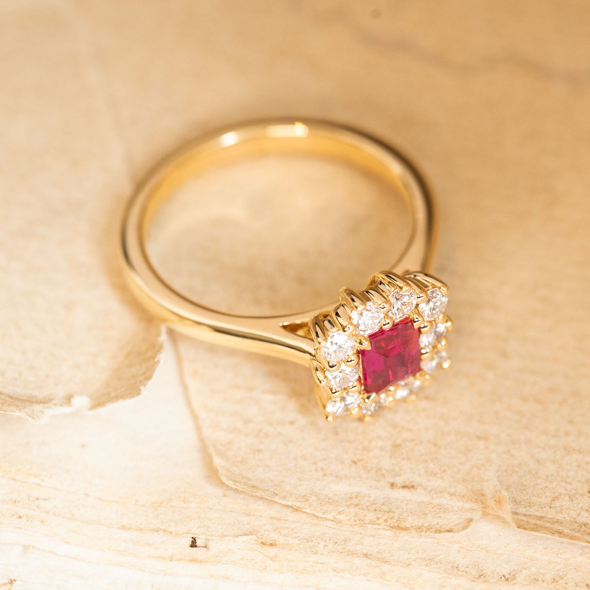 A rectangular step-cut ruby and diamond cluster engagement ring showcasing the raised setting and diamond halo.
