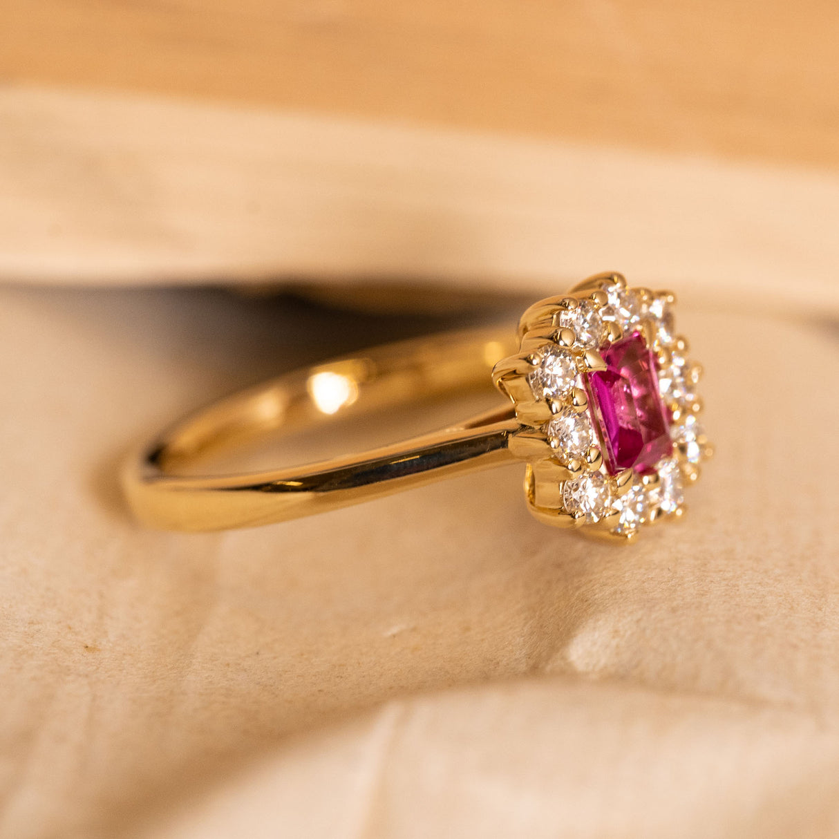Rectangular step-cut ruby and diamond cluster ring showcasing a rich red ruby framed by a sparkling diamond halo in yellow gold.