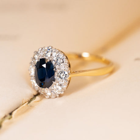 Vintage 1960s sapphire and diamond cluster ring showcasing an oval blue sapphire framed by a sparkling cluster of brilliant-cut diamonds.