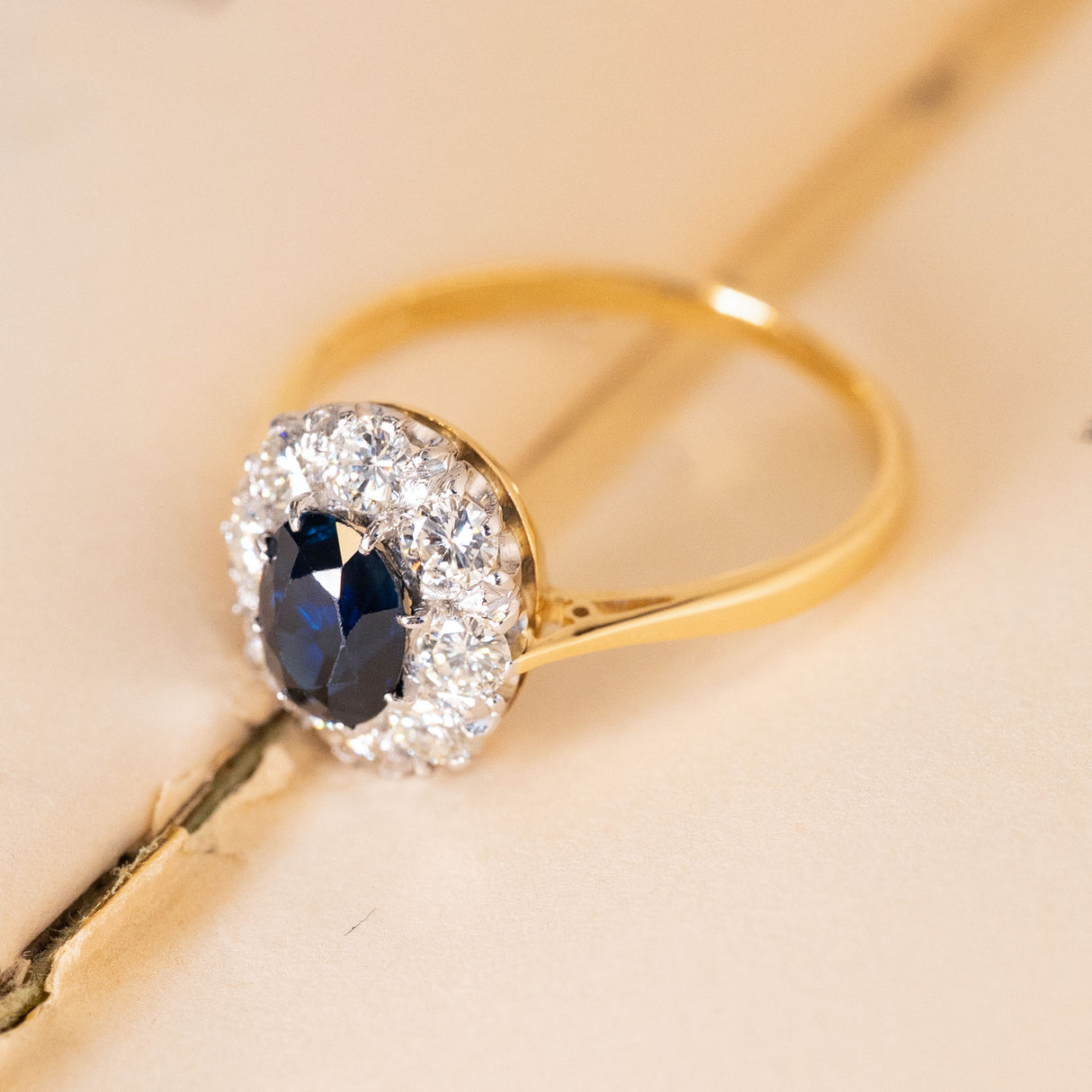 Vintage 1960s sapphire and diamond cluster ring displaying an oval blue sapphire within a brilliant-cut diamond cluster setting in yellow gold.