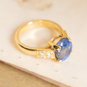 Vintage 1990s blue sapphire and diamond engagement ring with an oval-cut sapphire and channel-set diamond shoulders in yellow gold.