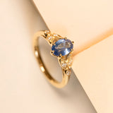Yellow gold engagement ring featuring an oval blue sapphire framed by intricate diamond-set yellow gold shoulders.