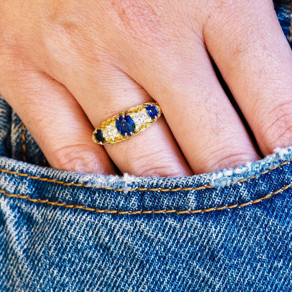 Close up of sapphire five stone ring worn with denim pocket detail.