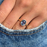 Antique-inspired yellow gold sapphire solitaire ring with an oval-cut slate blue sapphire, styled on hand against blue denim to highlight colour, scale and elegant simplicity.