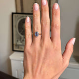 Antique-inspired yellow gold solitaire ring worn on hand, featuring an oval-cut slate blue sapphire in a sleek rub-over setting with a timeless, understated design.