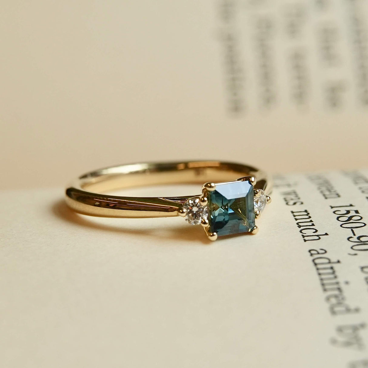 Square cut teal sapphire engagement ring with diamond three stone setting
