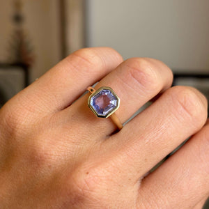 Close-up of an antique-inspired yellow gold sapphire solitaire ring showcasing a square lavender sapphire in a polished rub-over setting, highlighting its delicate pastel colour and elegant simplicity.
