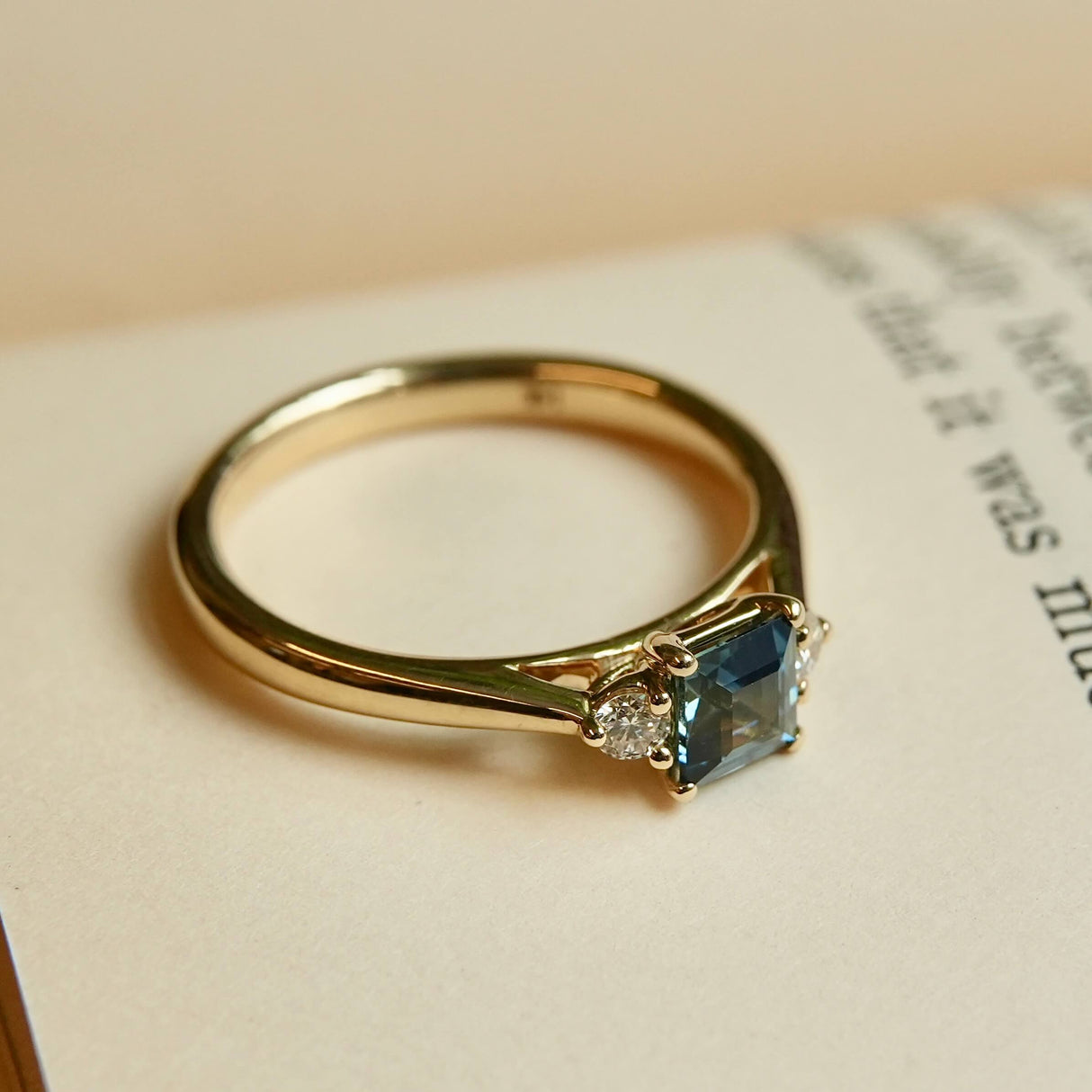 Square teal sapphire engagement ring with two diamond side stones