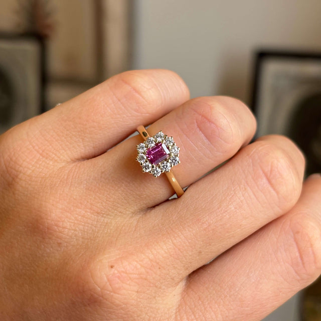 Close-up of an antique-inspired yellow gold cluster ring showcasing a step-cut pinkish-red ruby encircled by brilliant diamonds, highlighting colour, sparkle and fine craftsmanship.