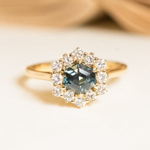 Teal hexagon-cut sapphire and diamond cluster engagement ring featuring a geometric teal sapphire surrounded by brilliant-cut diamonds in yellow gold.